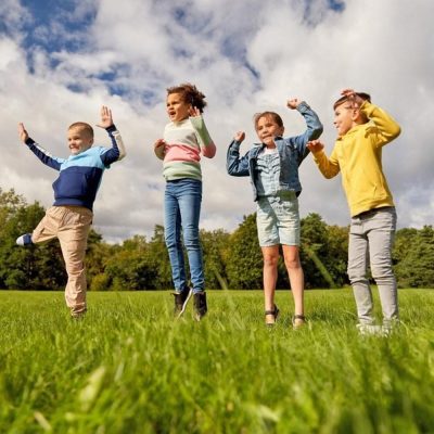 Group of four children jumping happily on grass under a bright sky